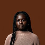 Portrait of young black girl looking into the camera on a brown blackground.