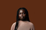 Portrait of young black girl looking into the camera on a brown blackground.