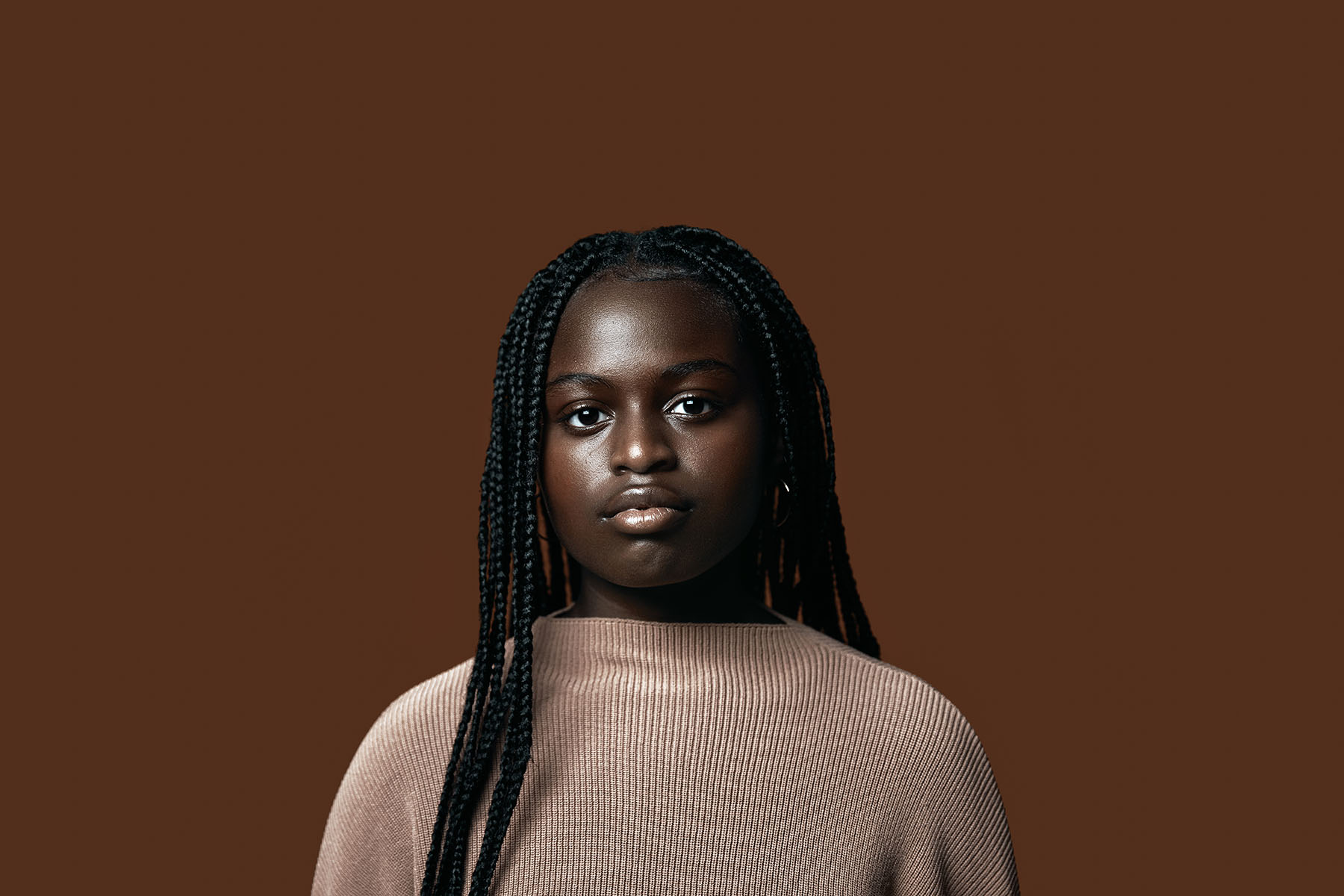 Portrait of young black girl looking into the camera on a brown blackground.