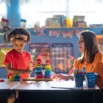 A preschooler plays with toys beside her teacher.