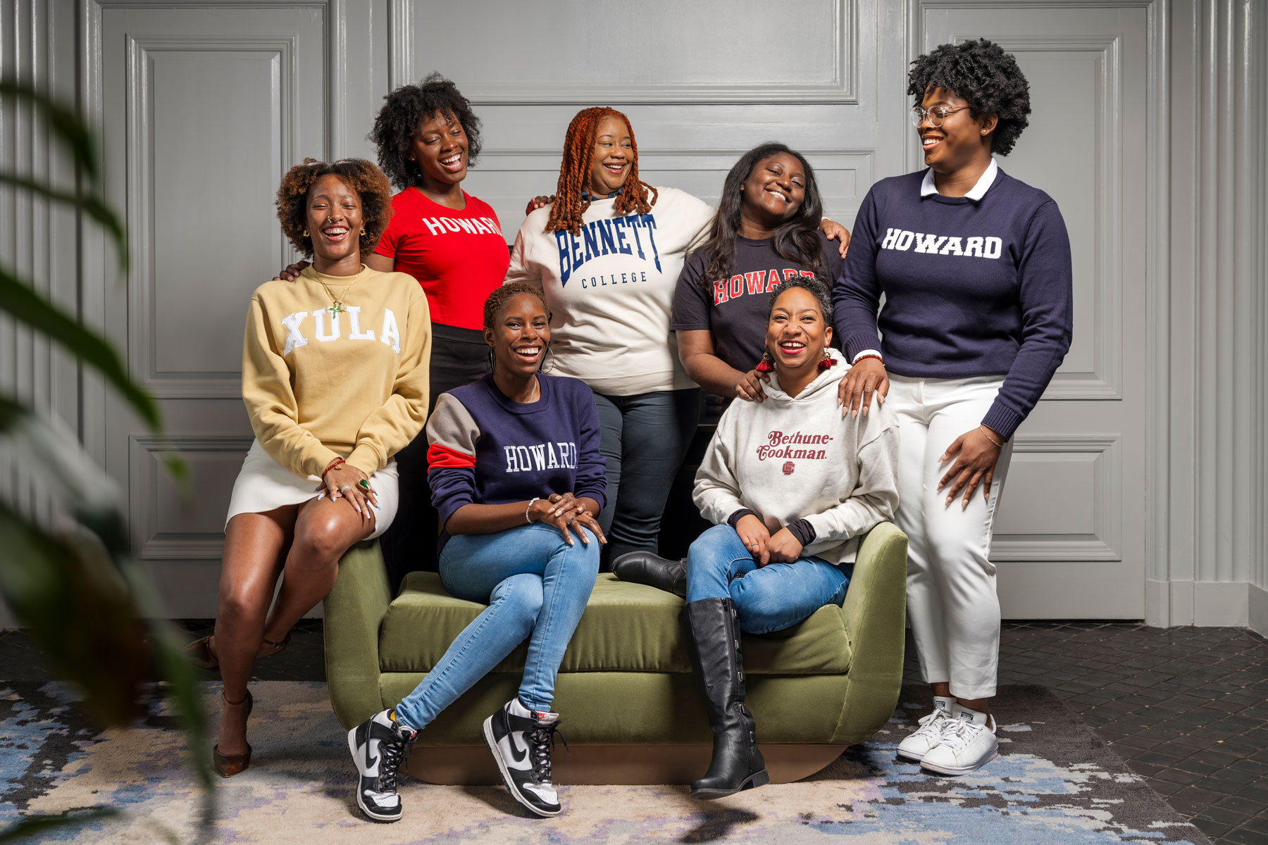 A group of fellows wearing HBCU sweatshirts standing around a green couch where their program mentors are seated.