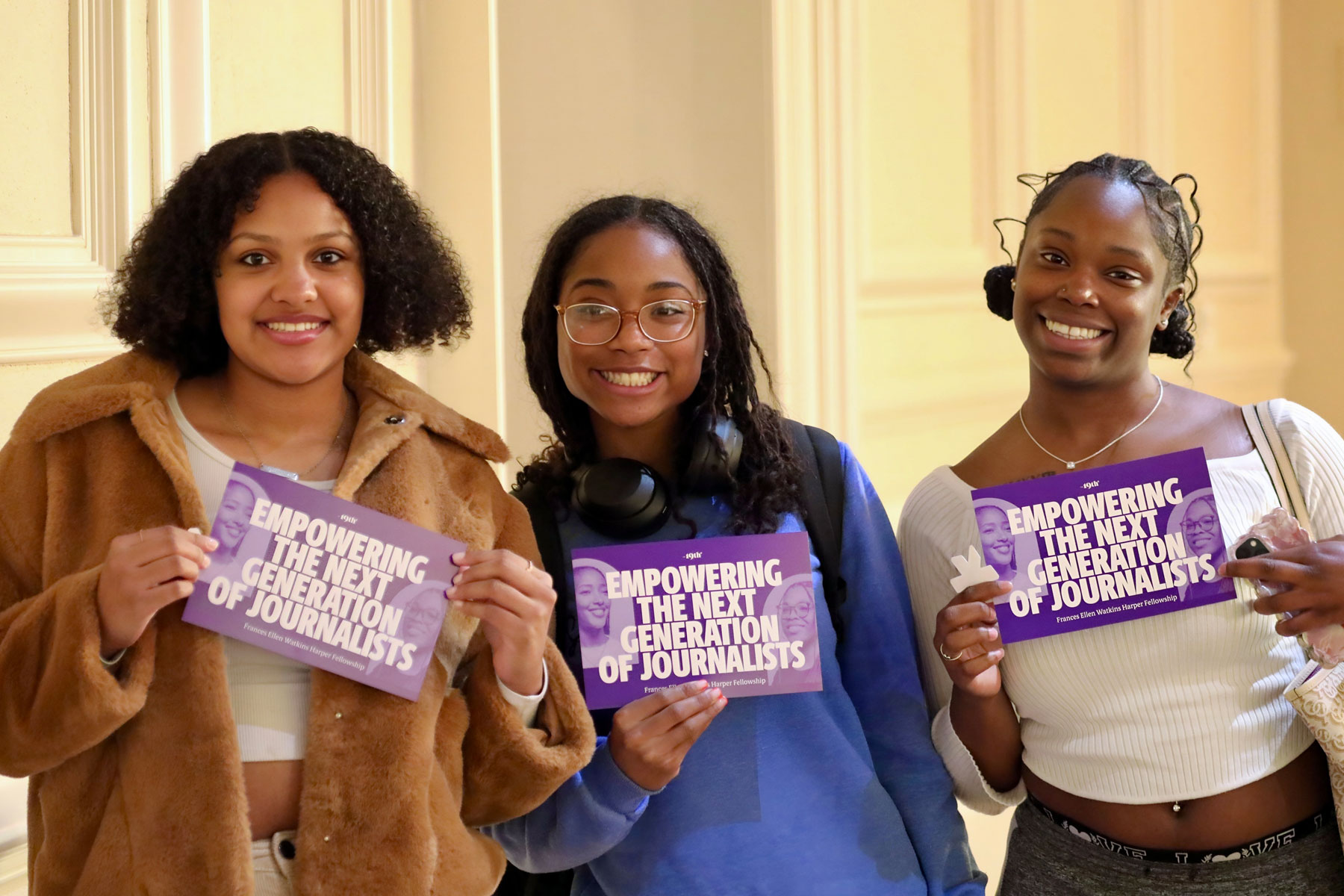 A group of three smiling Spelman students holding 19th Fellowship postcards.