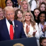 A crowd of women clap and smile behind Trump.