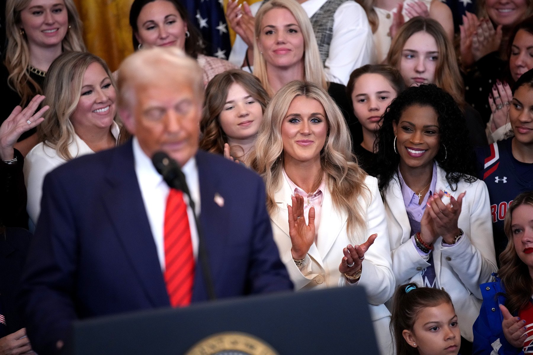 A crowd of women clap and smile behind Trump.