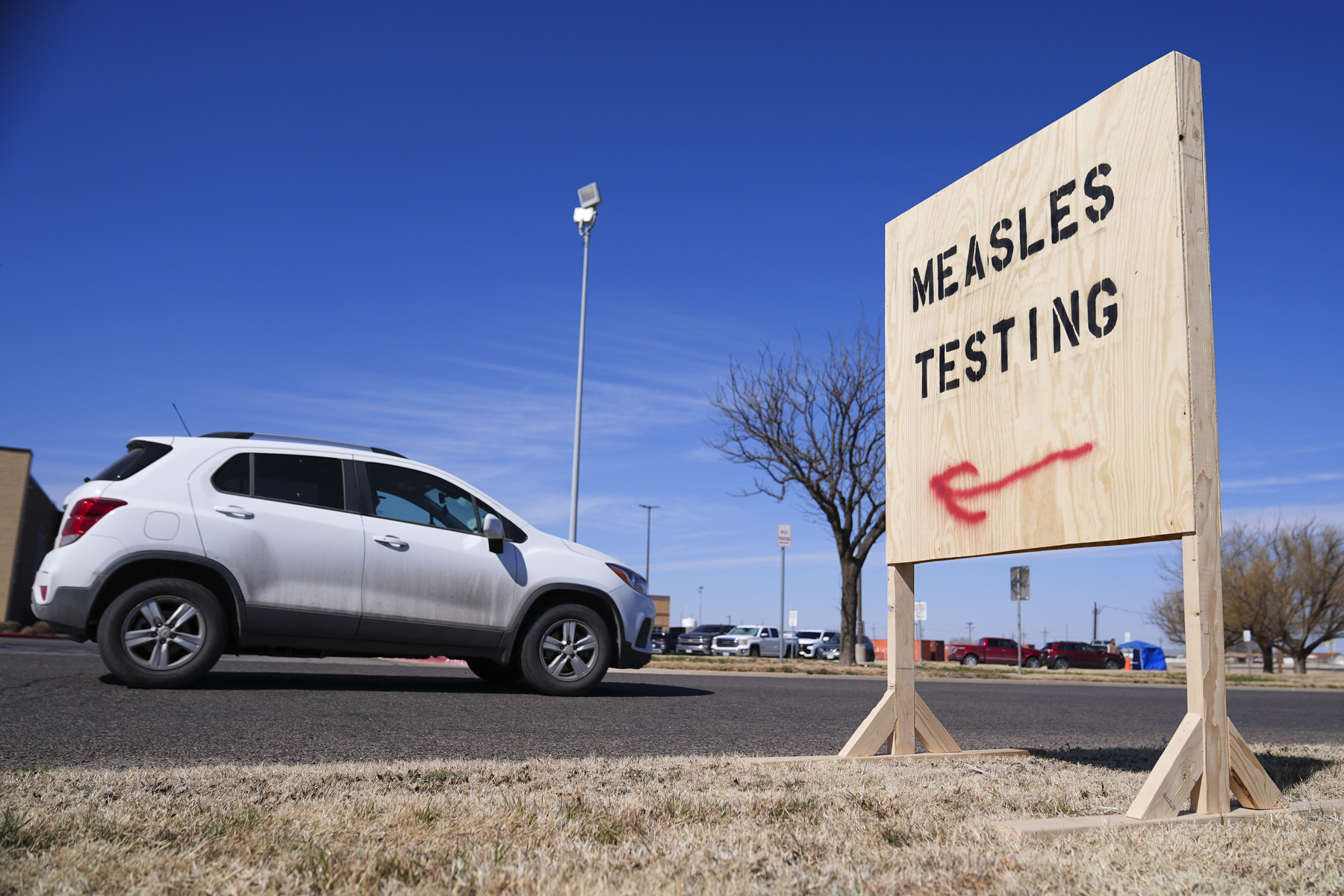 A white car drives past a sign pointing to a measles testing site.