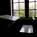 Antique white school bench in a dark classroom lit by ambient sunlight from a window.