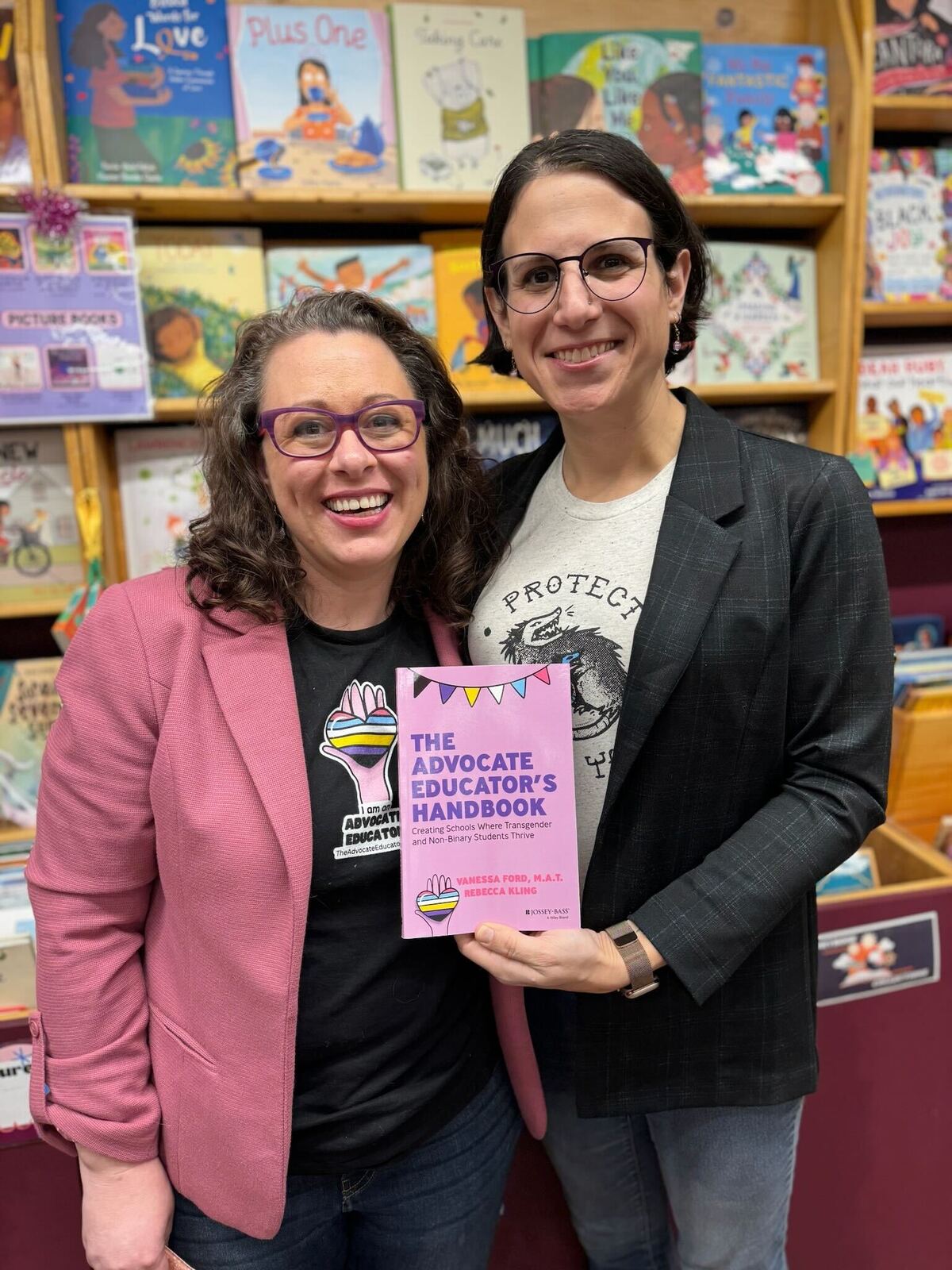 Two people stand in a bookstore and pose for a photo while holding a book.