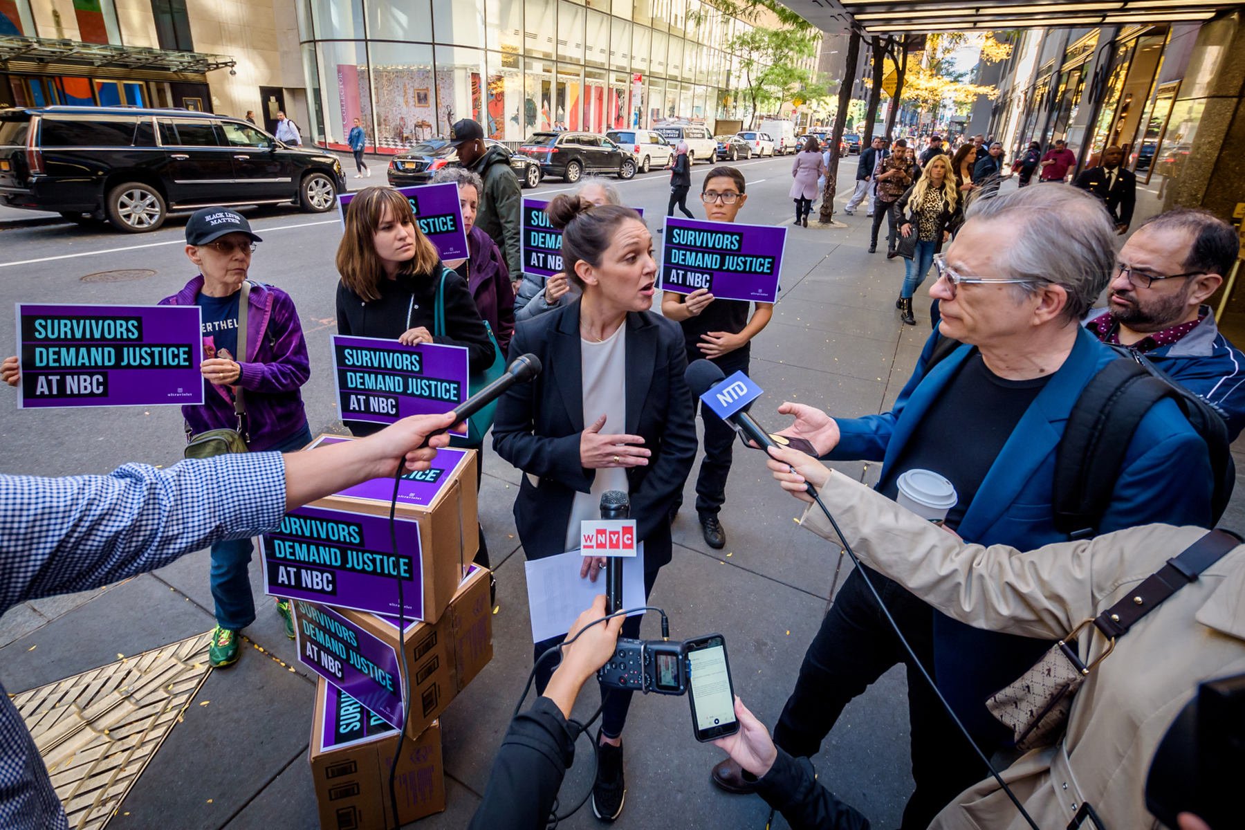 A group of protestors are interviewed by journalists with microphones in outstretched hands.