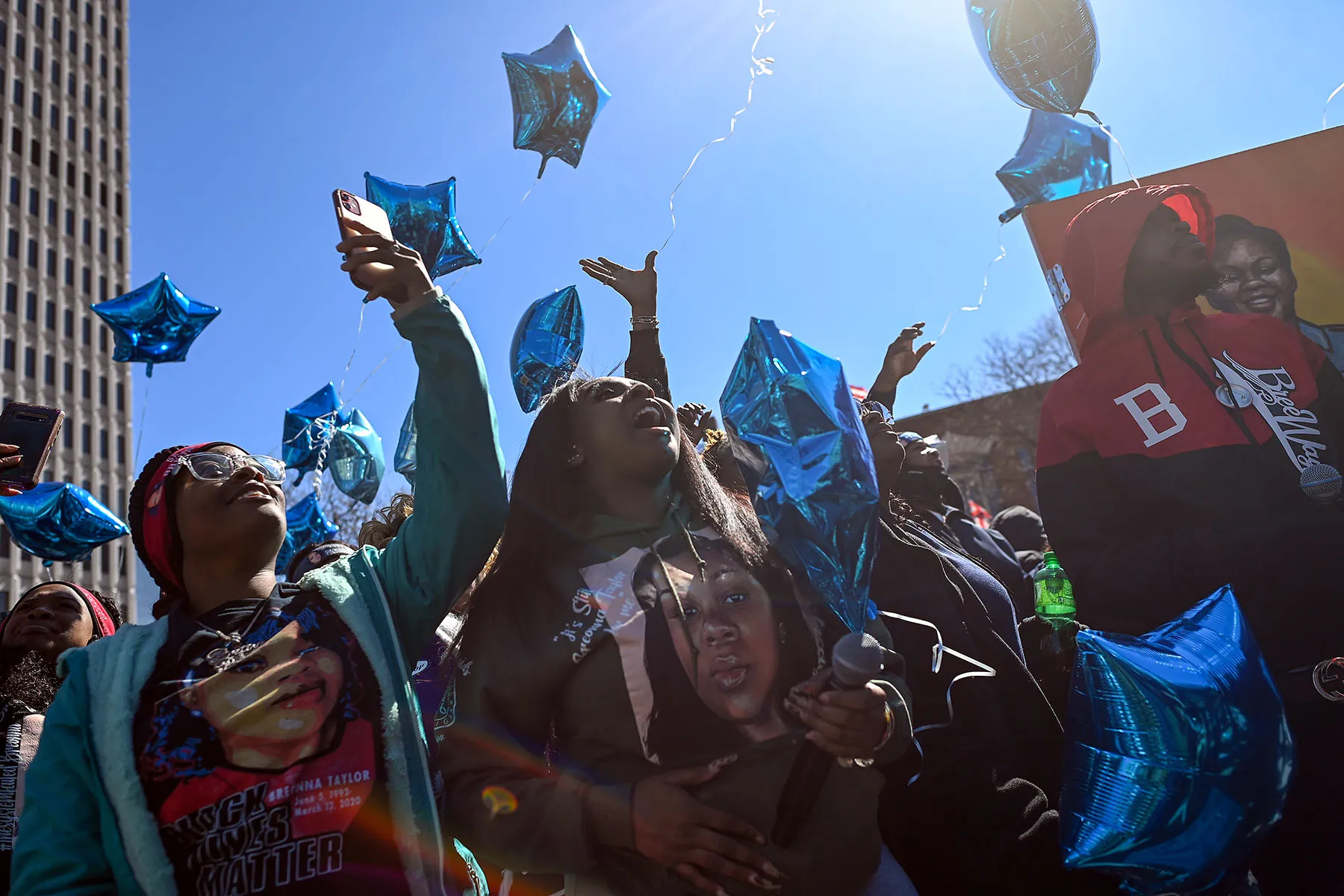 Preonia Flakes (izquierda) y Kori Baskin (Centro) se reúnen en Jefferson Square Park para un balón de lanzamiento de globos en forma de estrella azul en el segundo aniversario de la muerte de Taylor.