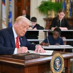 President Donald Trump signs an executive order surrounded by children at school desks also signing fake executive orders in the East Room of the White house.