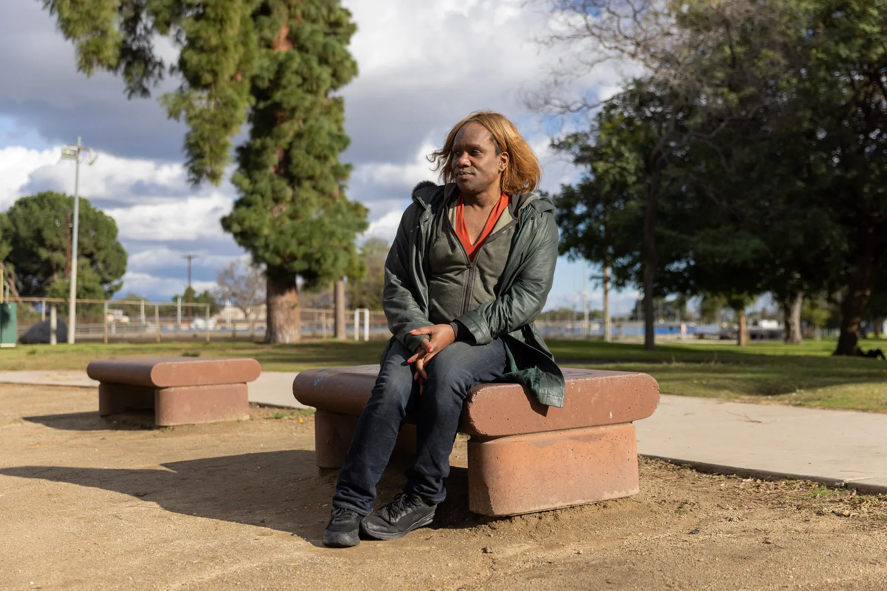 A woman sits on a bench in a park.