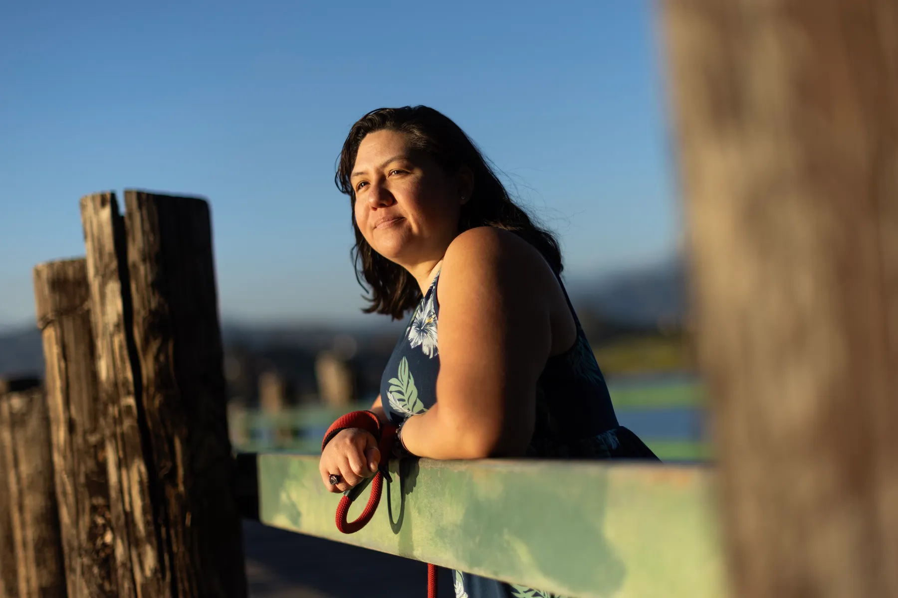 A woman leans over a railing with the sun shining on her face.