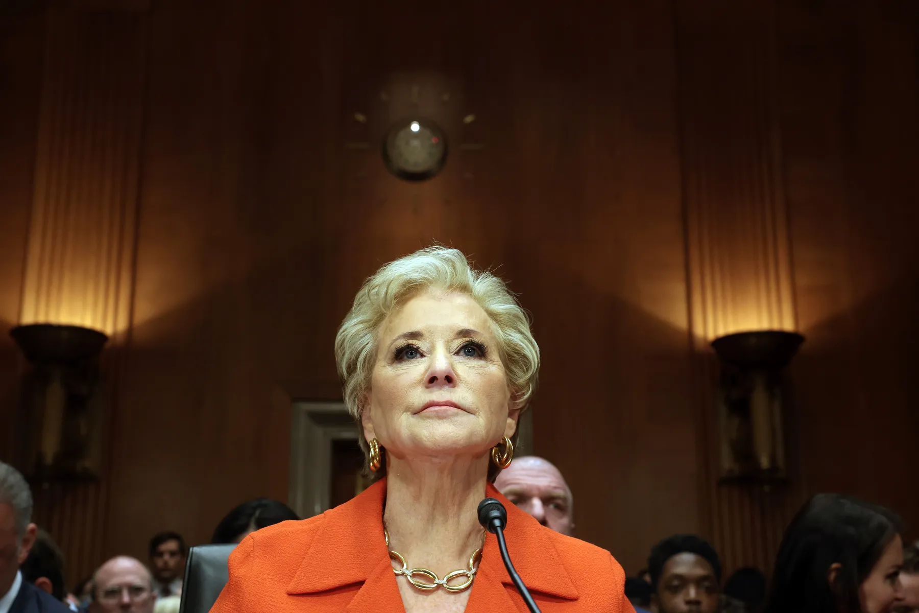 A woman sits at a microphone, unsmiling.