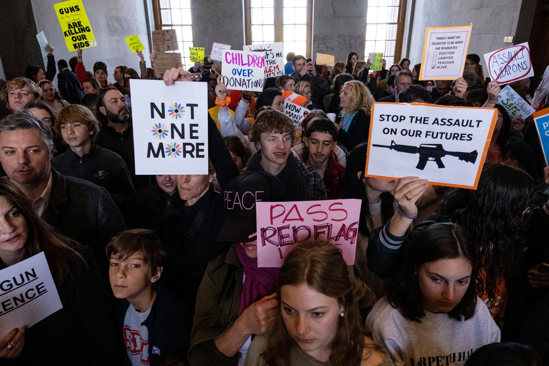 A group of protestors, many of them children, hold up anti-gun violence signs.