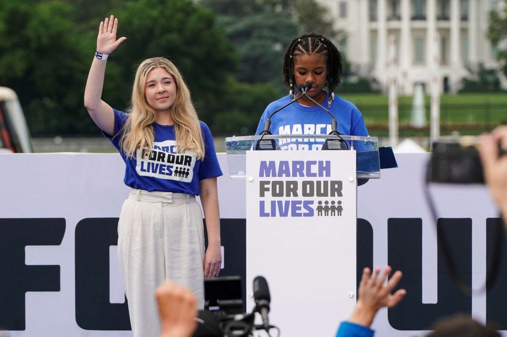 Two women stand at a podium while people in a crowd raise their hands in front of them.