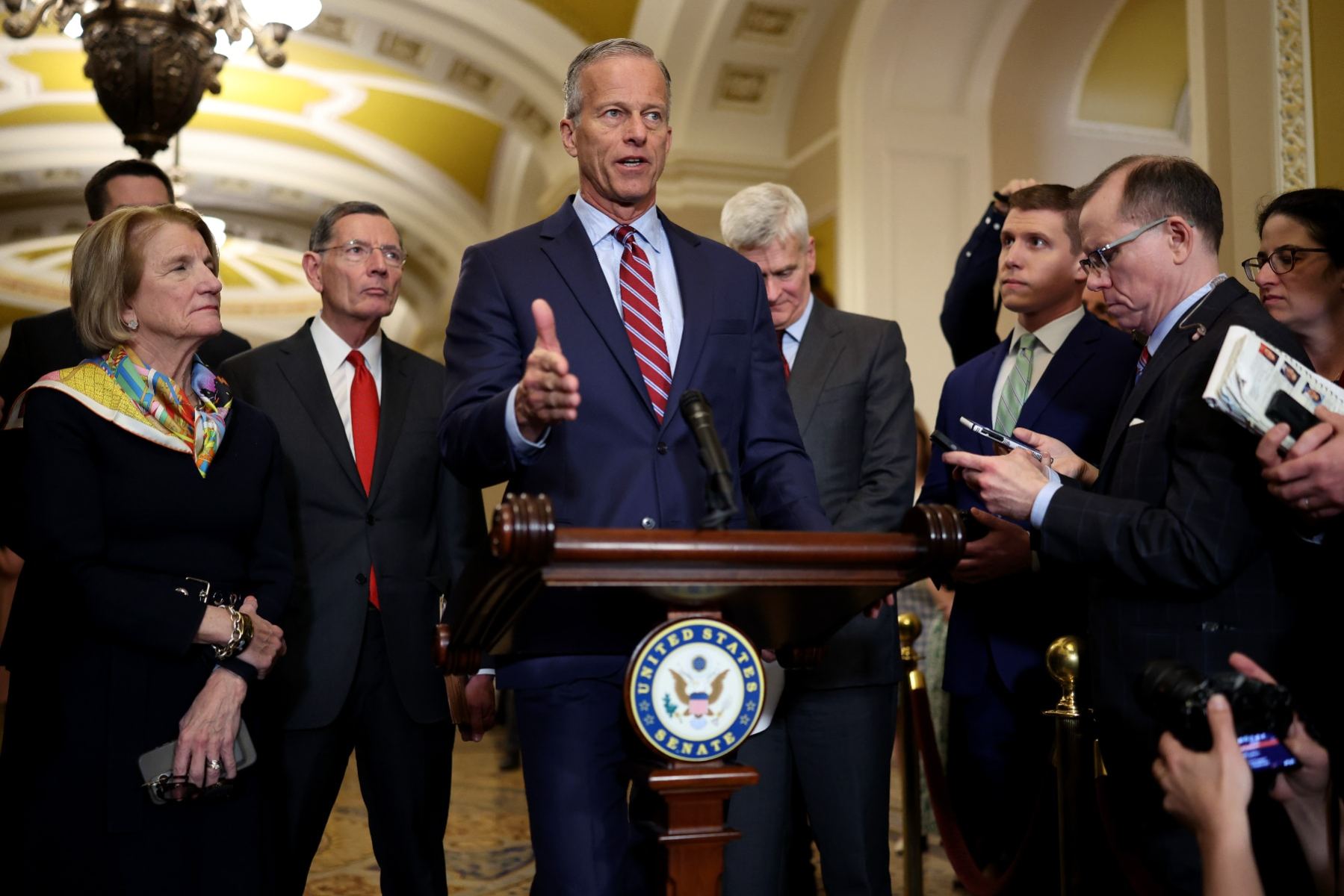 Sen. John Thune stands at a lectern and speaks to reporters