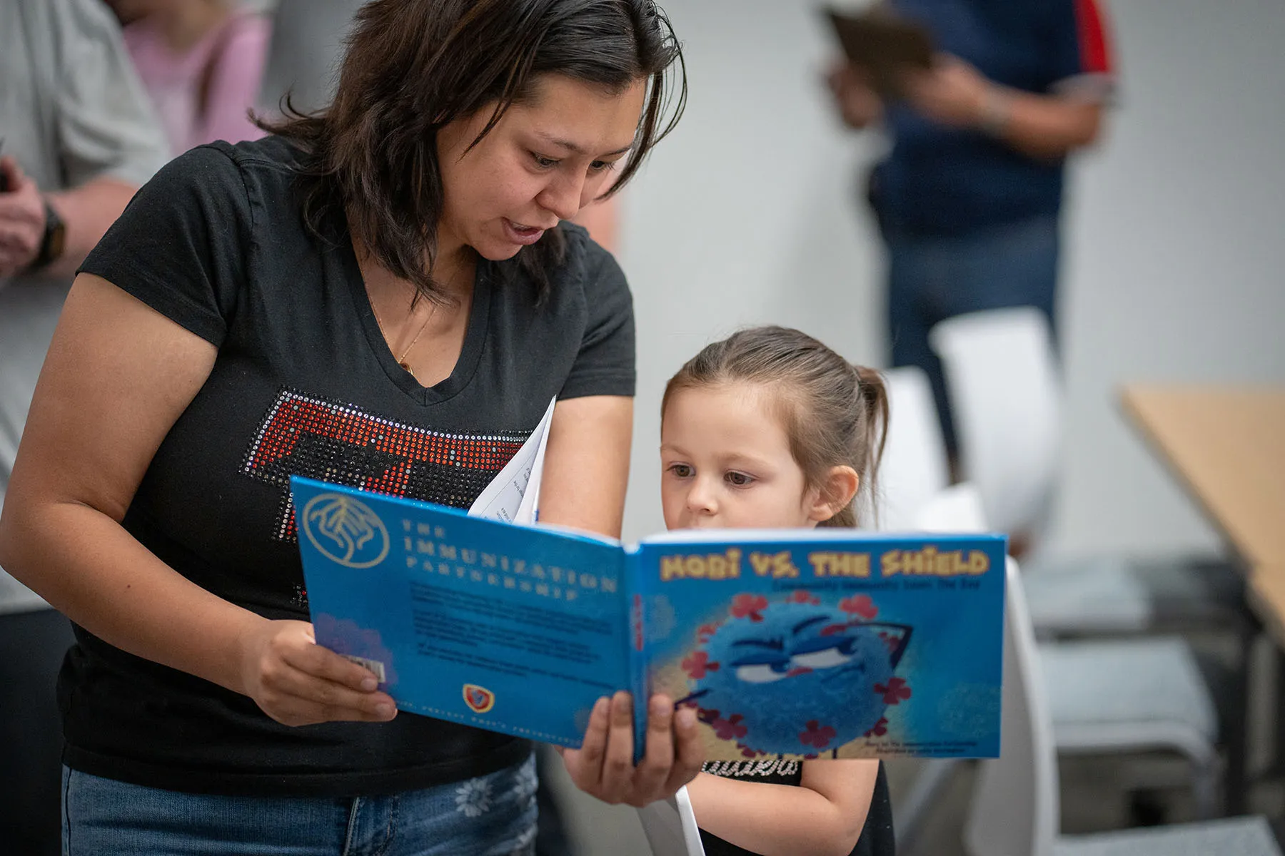 A parent reads a book about immunizations with their child at a vaccine clinic.