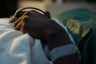 Close-up of a person's hand resting on a hospital bed, with a medical wristband and monitoring clip attached to their finger.