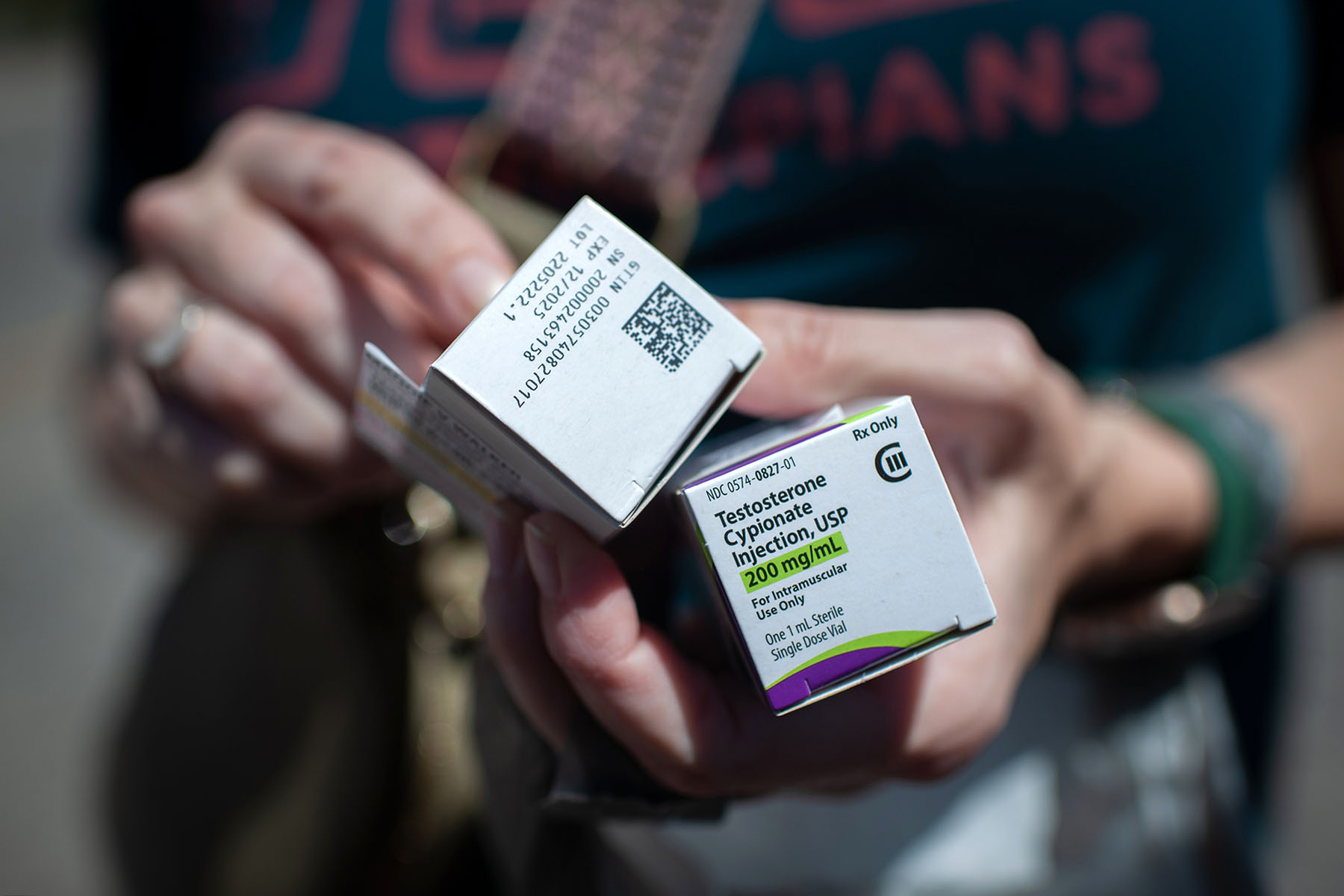 A person holds boxed testosterone prescriptions.