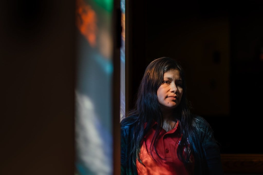 Yessenia Ruano stands in front of a stained-glass window, her face lit by the colors.