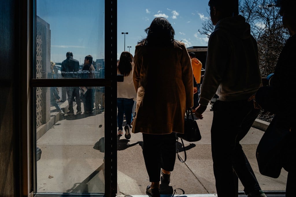 A crowd walks out of a church doorway into the daylight after mass.