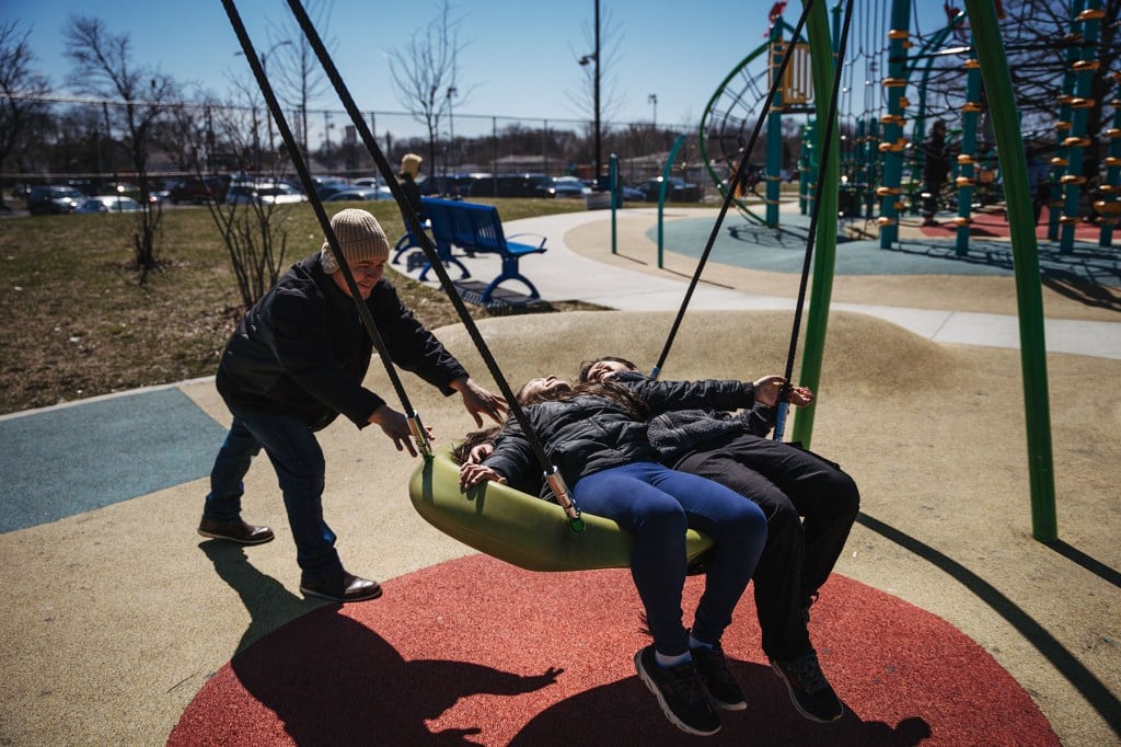 Miguel plays with Elizabeth and Paola on a swing at the park.