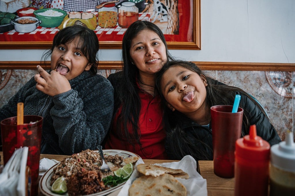 Yessenia Ruano sits at a restaurant table with her daughters, who smile and stick out their tongues.