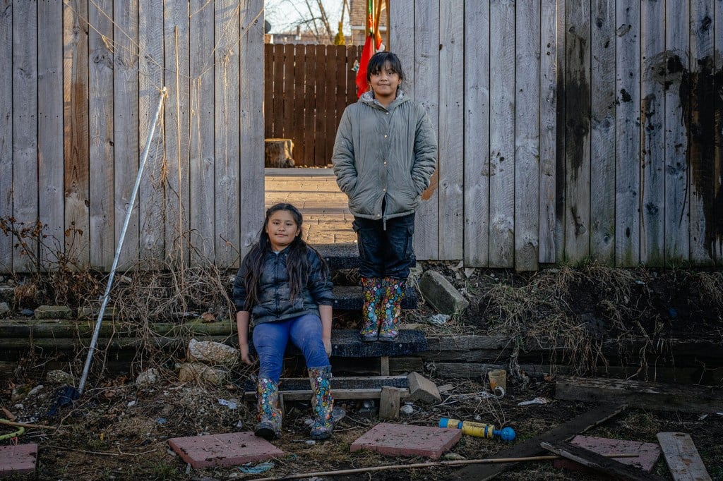 Elizabeth and Paola pose outside near their backyard fence in rubber boots.