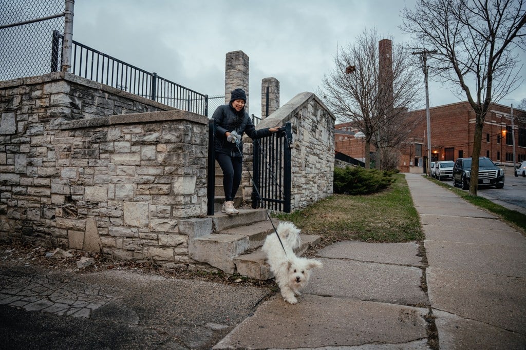 Yessenia Ruano walks down stone steps with her dog on a leash in front of a brick building.