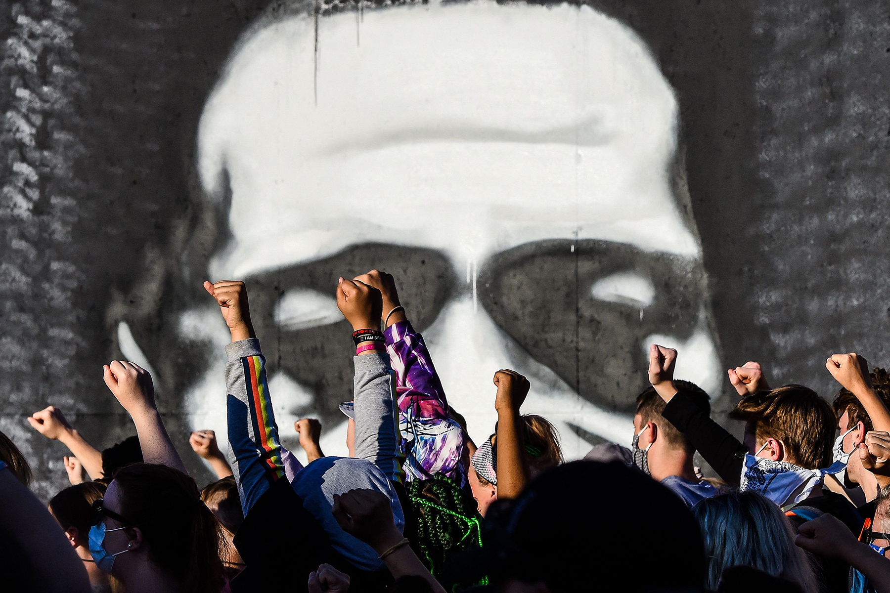 Protestors raise their fists in the air against the backdrop of a George Floyd mural.