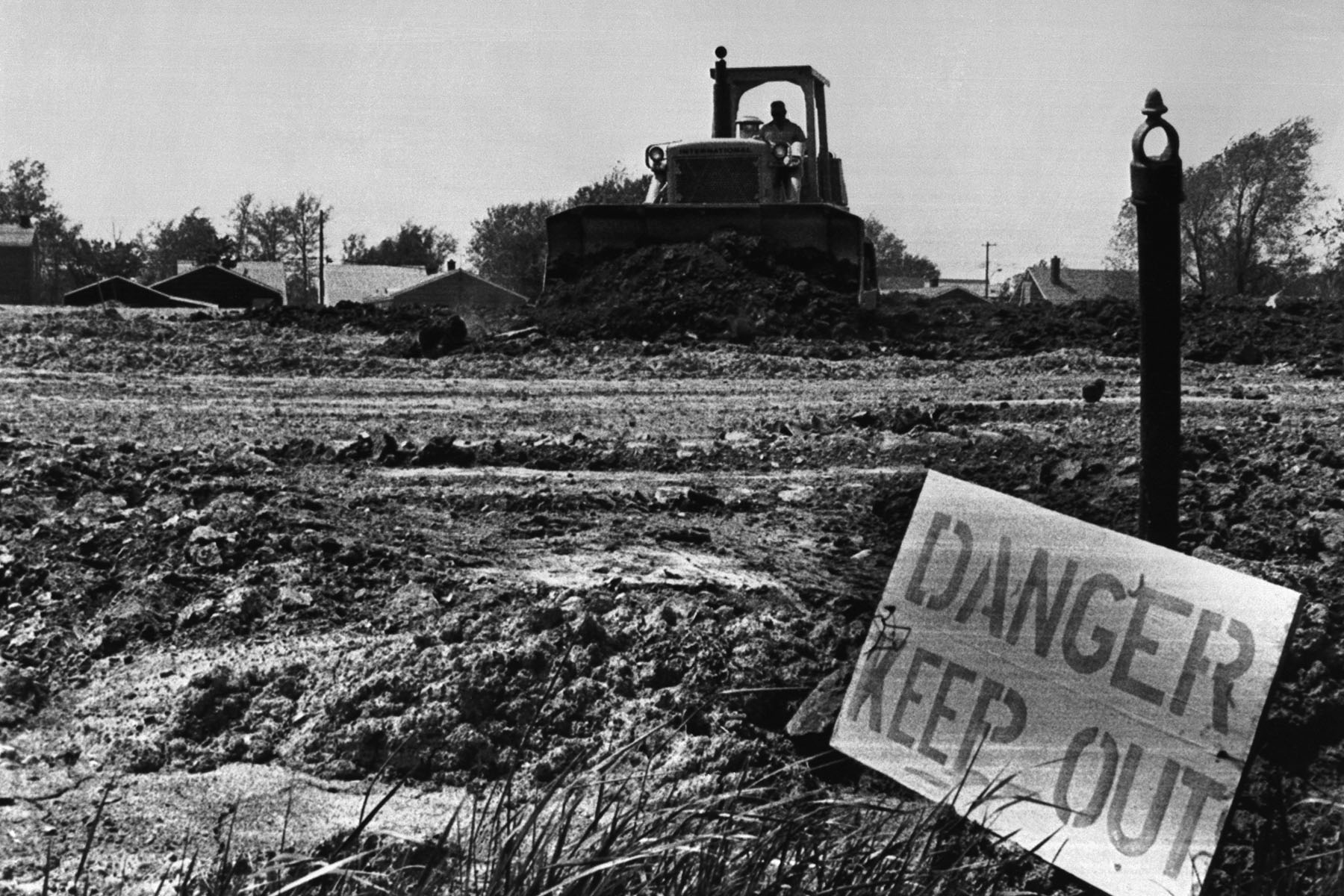 A bulldozer moves dirt at Love Canal in May 1980, with a “Danger Keep Out” sign posted in the foreground during early cleanup efforts.