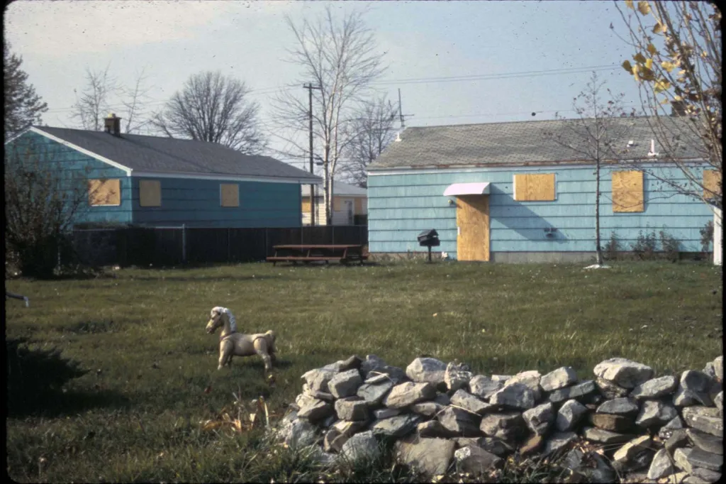 A backyard in Love Canal in 1978 with a toy horse in the grass and homes boarded up after residents evacuated.