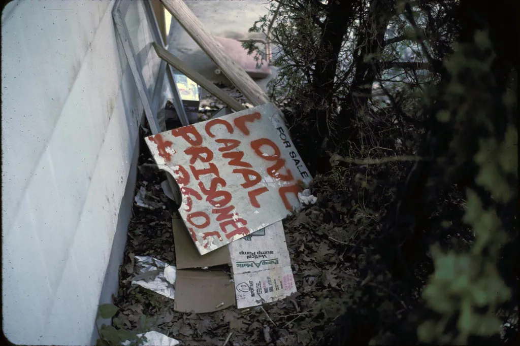 A hand-painted protest sign reading “Love Canal Prisoner” sits atop demolition debris in the neighborhood in 1982.