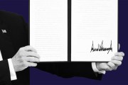 A close-up of President Trump holding open a signed executive order with a large signature visible on the right page.