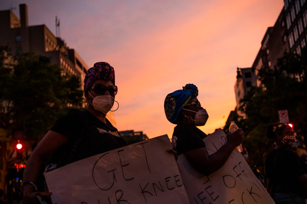 Black women protestors march in the streets against a sunset.