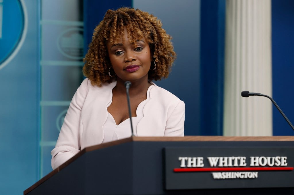 Karine Jean-Pierre listens as she stands at a podium.