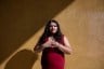 Angélica Reyes stands with her hands over her chest in front of a textured yellow wall.