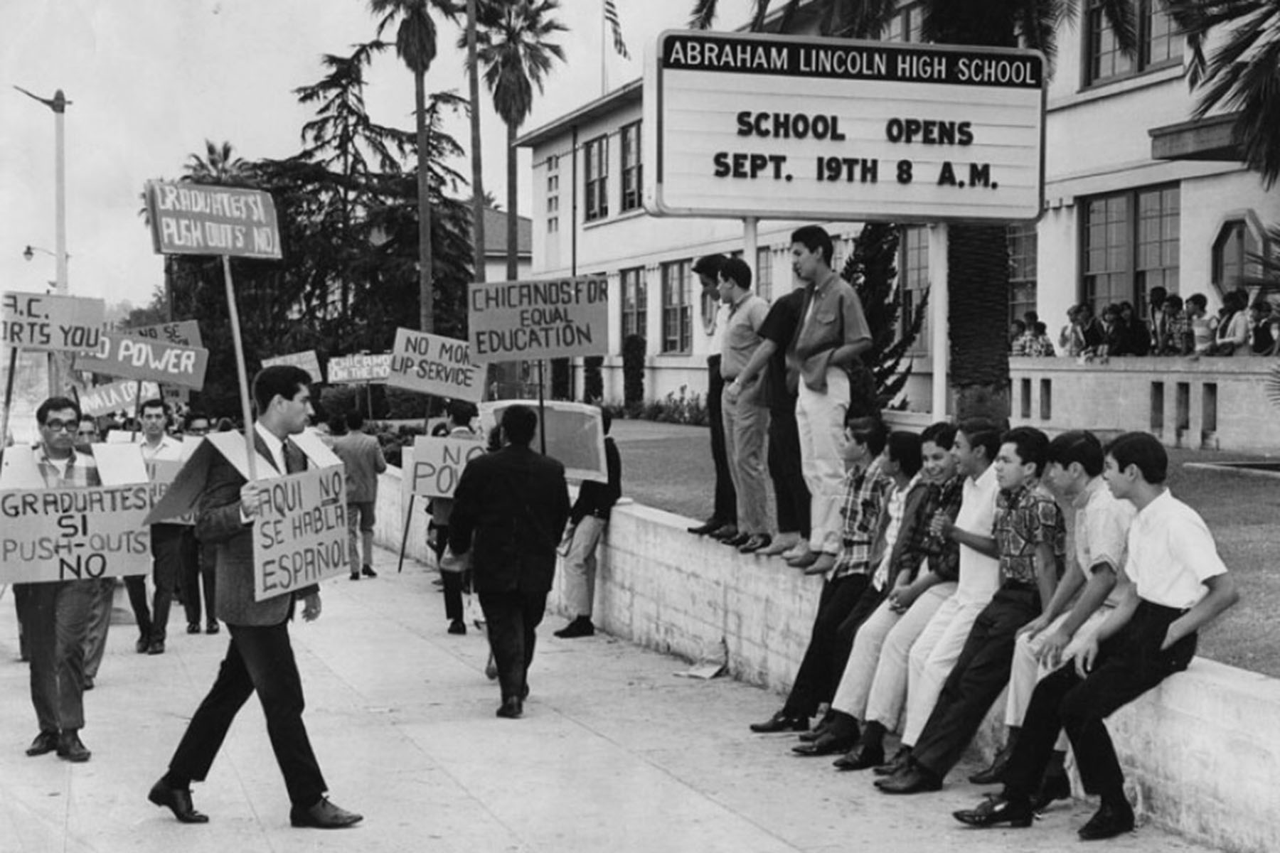 Black-and-white photo of students holding protest signs outside Abraham Lincoln High School demanding equal education and language rights.