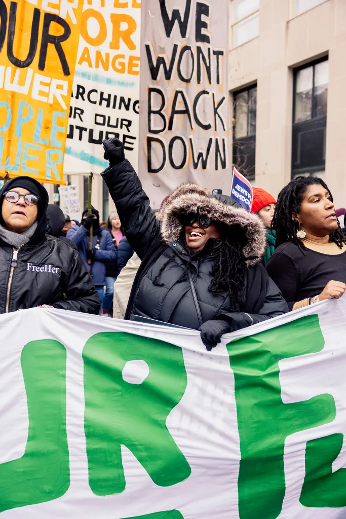 A smiling woman raises her fist in the air at a protest.