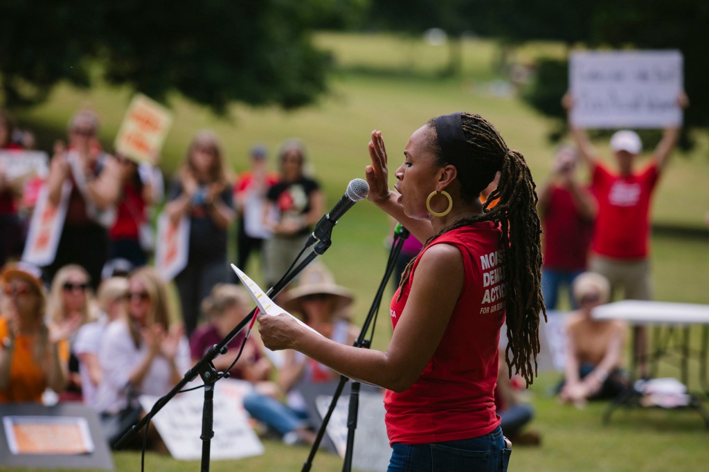 A woman speaks at a microphone during a protest.