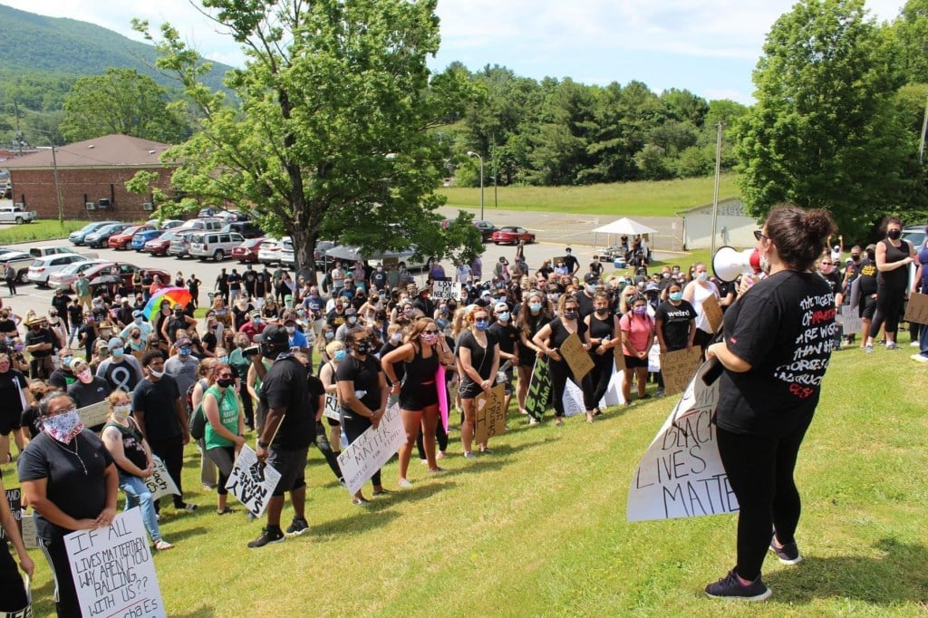 A group of protestors stand on a hill listening to a person with a bullhorn.