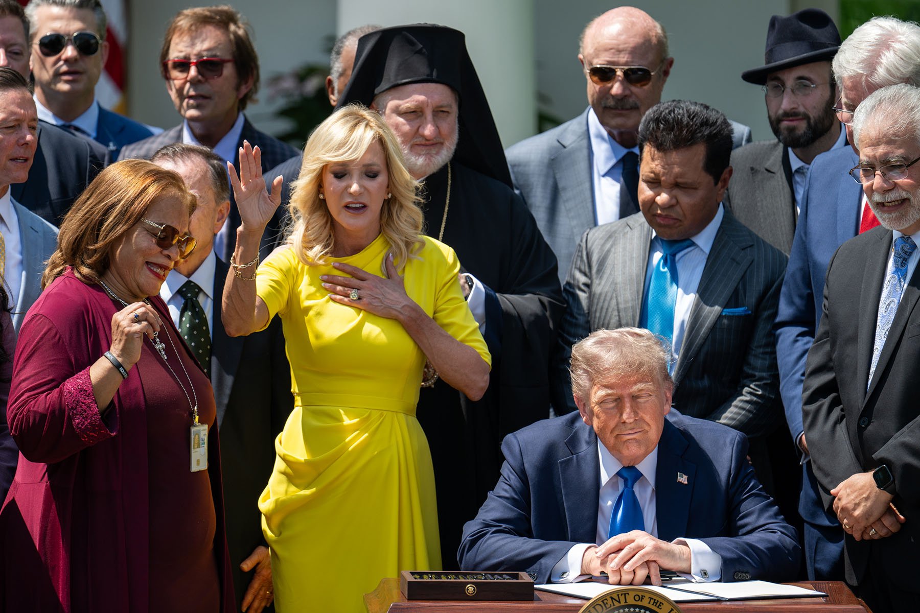 Donald Trump sits at a desk in the White House Rose Garden as religious leaders and supporters gather behind him