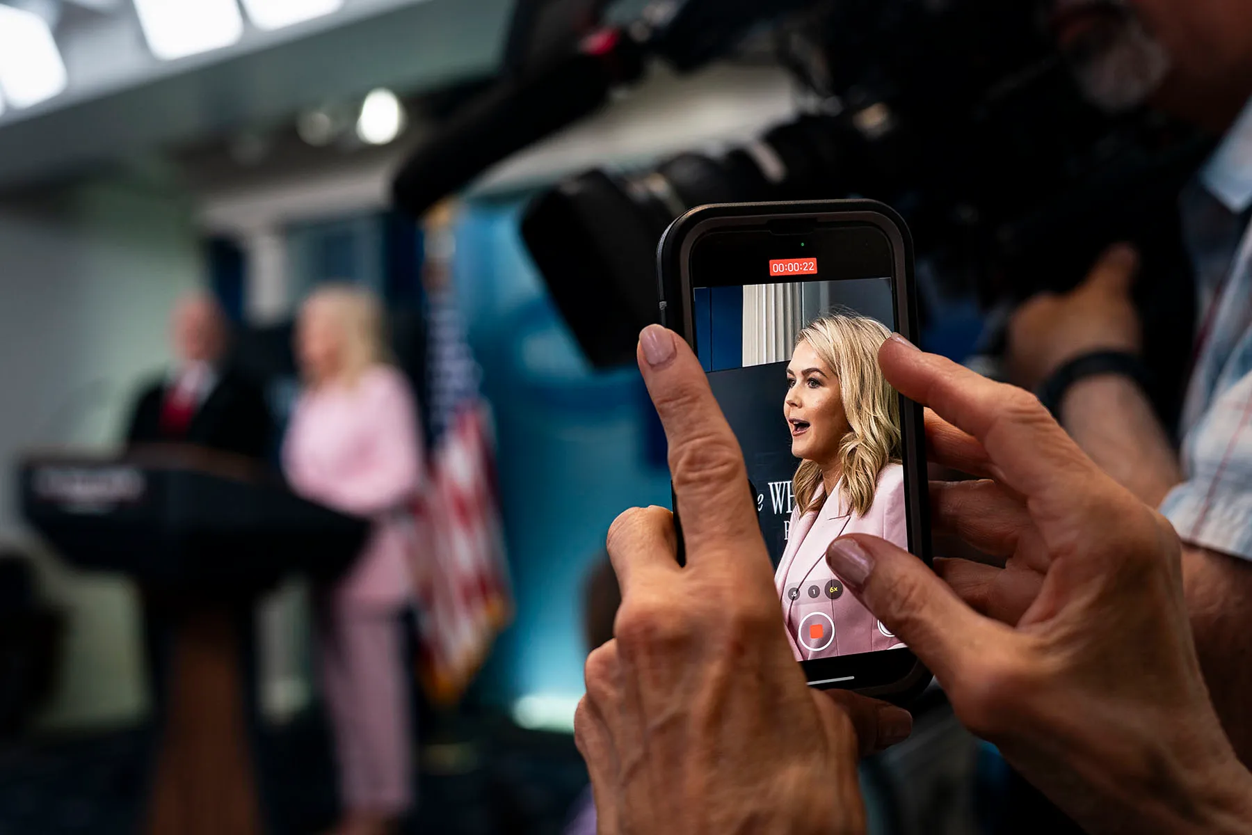 A person records White House Press Secretary Karoline Leavitt on their phone as she speaks at a press briefing.