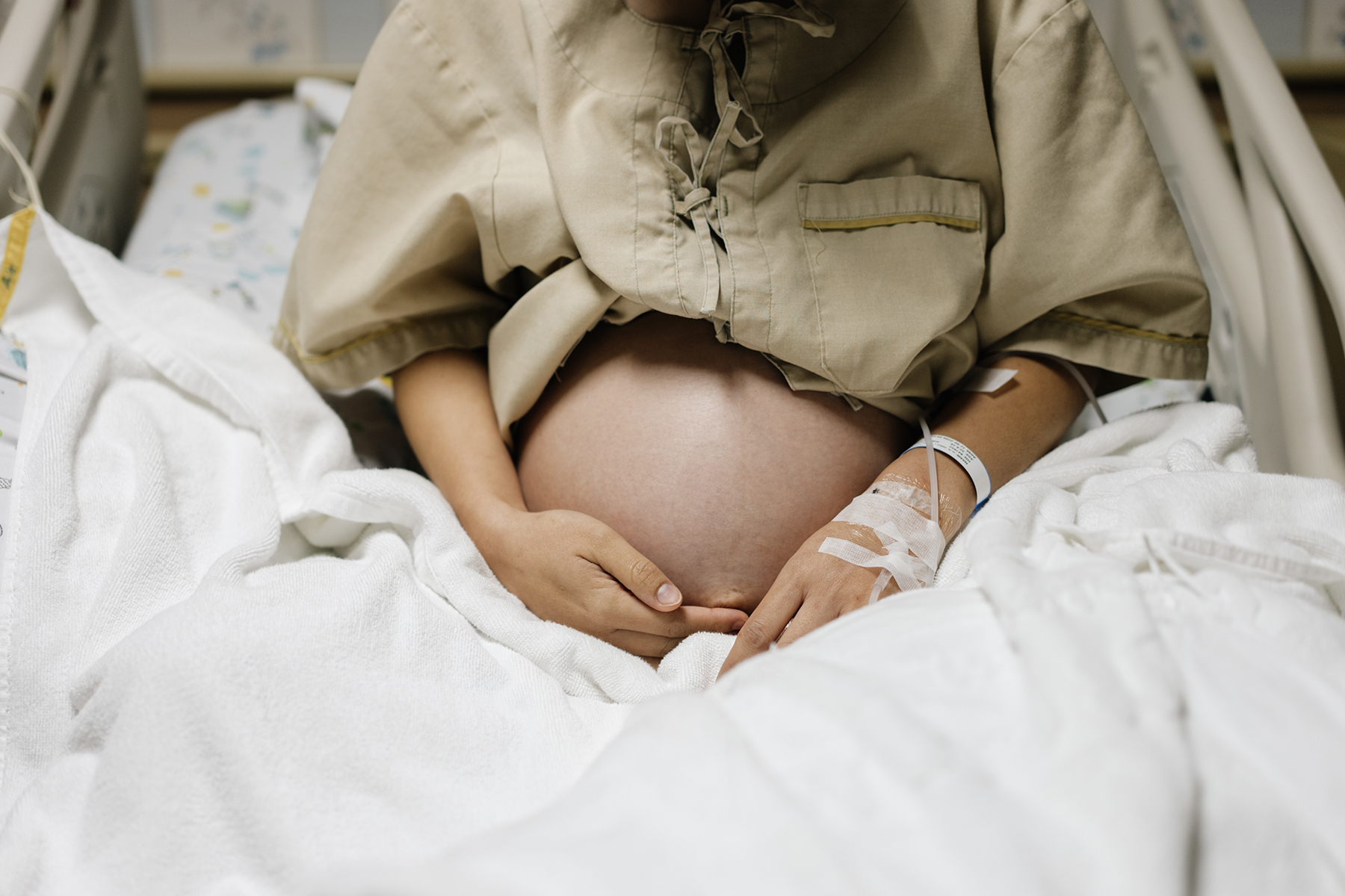 A pregnant person sits in a hospital bed wearing a hospital gown.