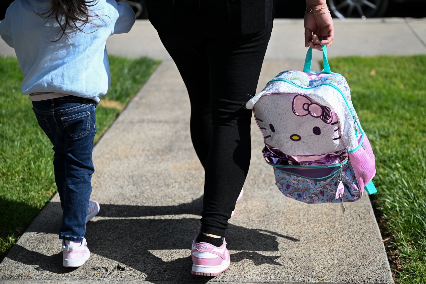 A mother holds her child's backpack and her child's hand.