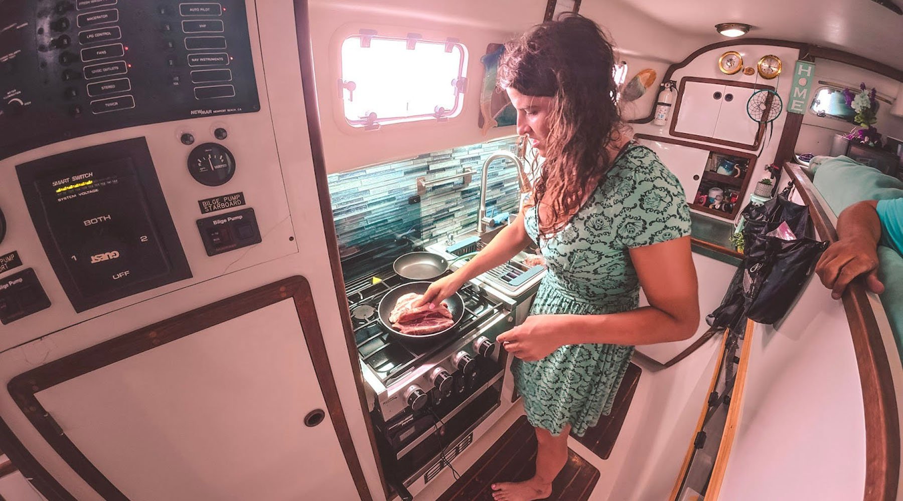 Kelsey Granger cooks meat in a pan on a stove inside a sailboat galley.