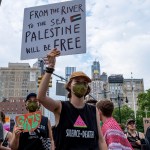 A person wearing a mask holds up a sign supporting Palestine during a march.