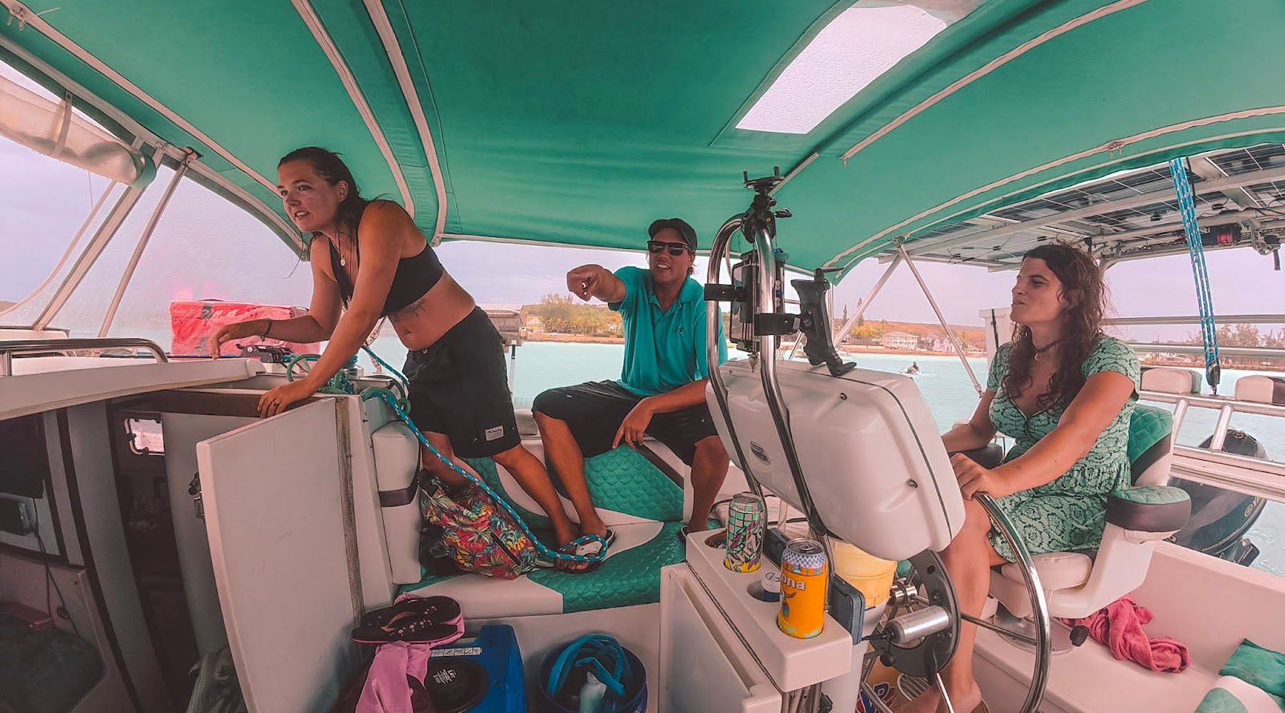 Three people sit under the green canopy of a sailboat cockpit, including Kelsey Granger.