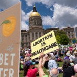 Protestors raise signs in front of the Georgia state capitol building.