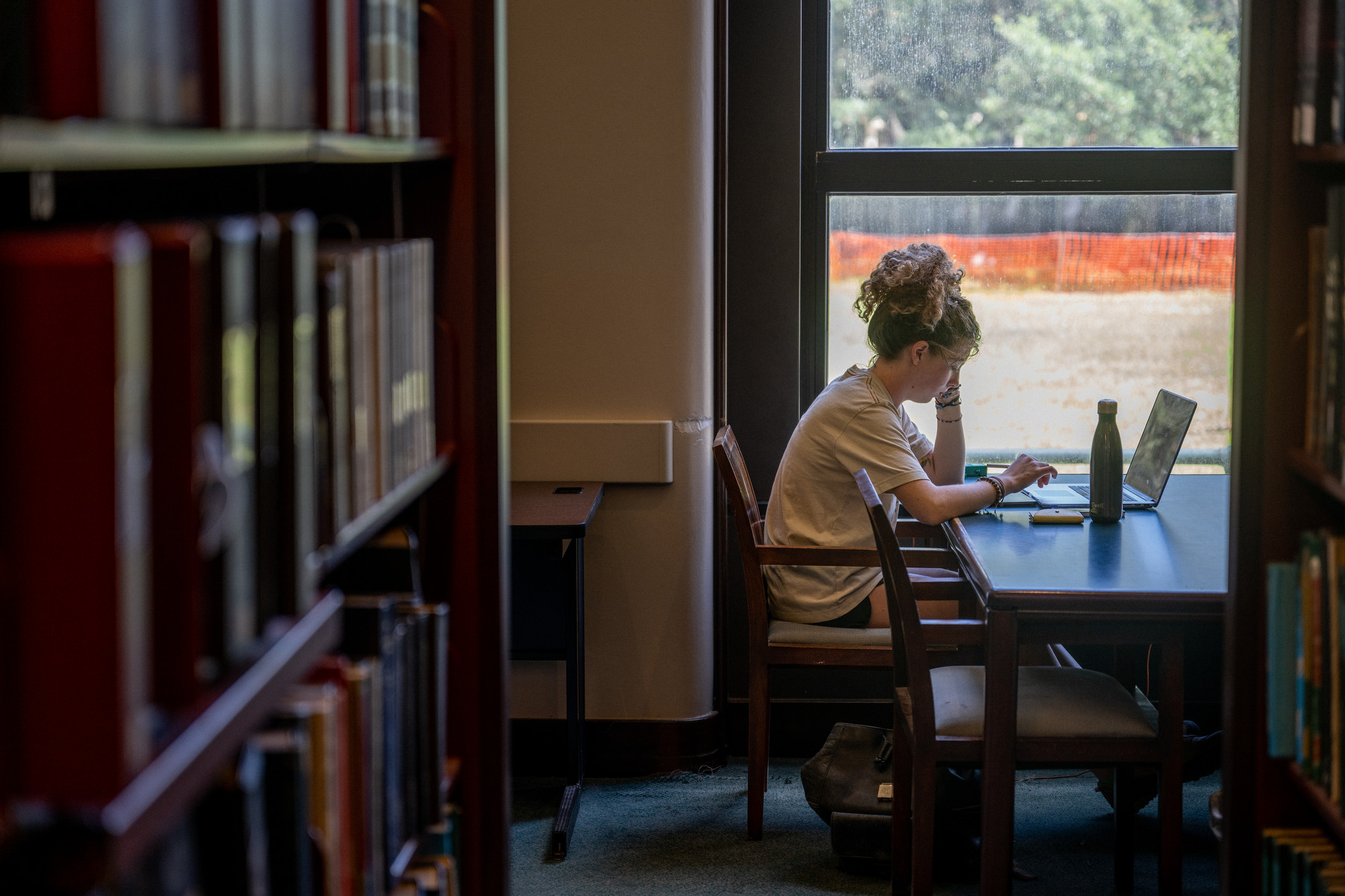 A students sits at a desk in a college library.